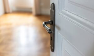 Door open close up. Retro doorknob on white door, blur floor parquet, classy room interior